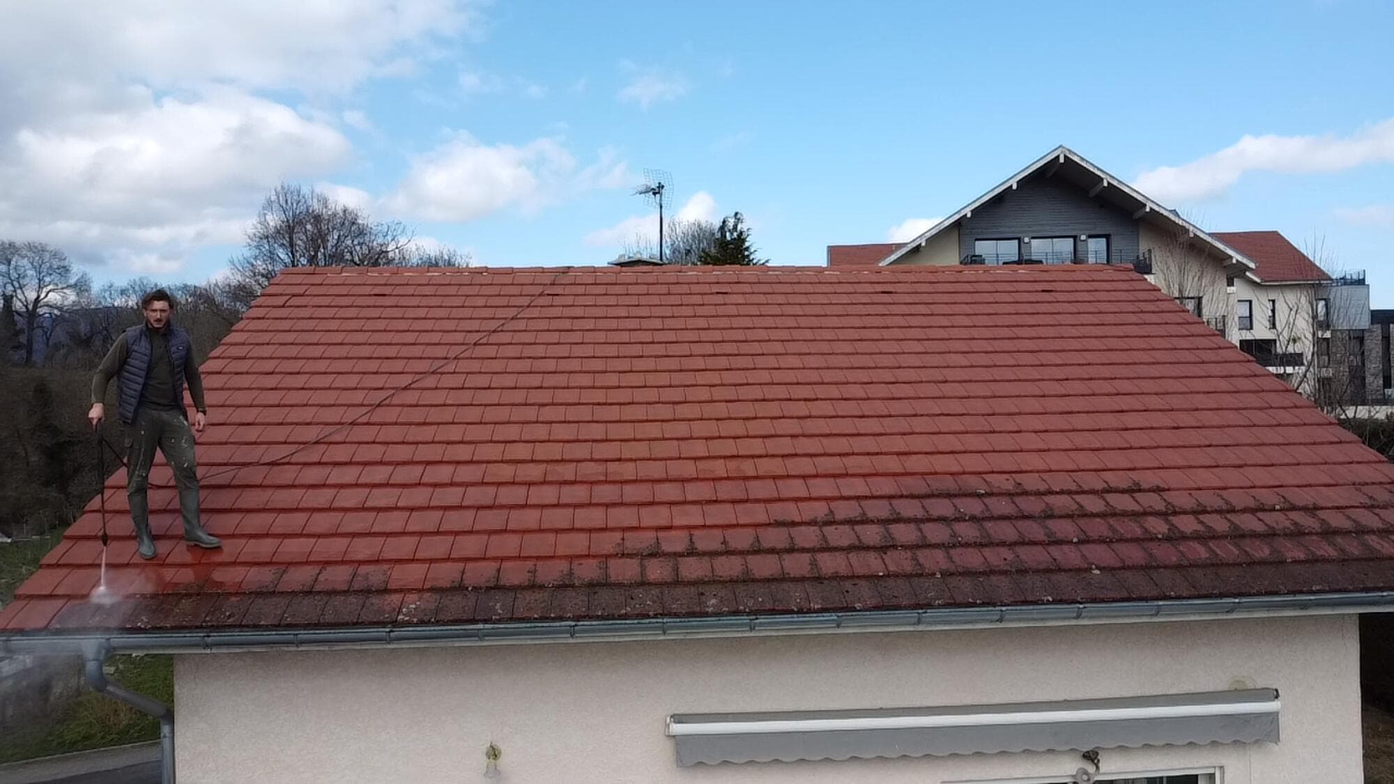 Artisan PROUX nettoyant une toiture en tuile au nettoyeur haute pression, vue sur les montagnes du Pays de Gex